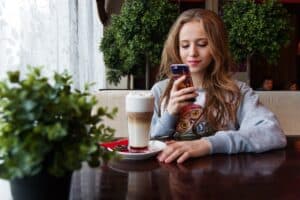 młoda dziewczyna w kawiarni z telefonem i kawą