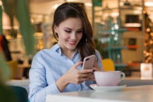 uśmiechnięta kobieta przeglądająca telefon siedząc przy kawie
